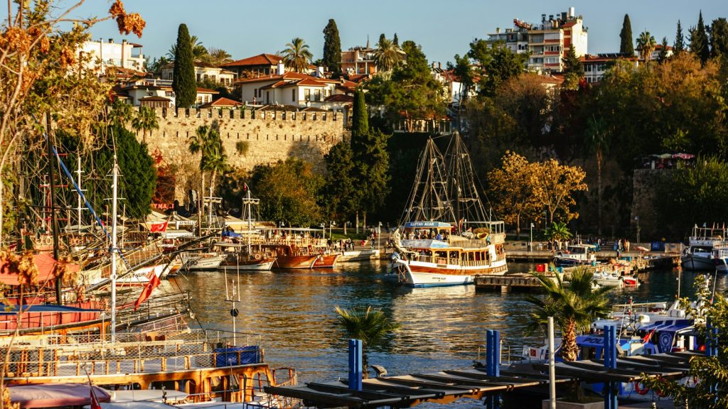 Hajók Antalya régi kikötőjében, fölötte a Kaleiçi óváros házai és falai