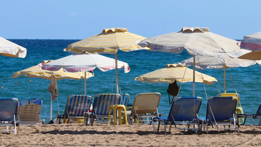 Napernyők és nyugágyak egy rodoszi homokos strandon, kék tengerrel