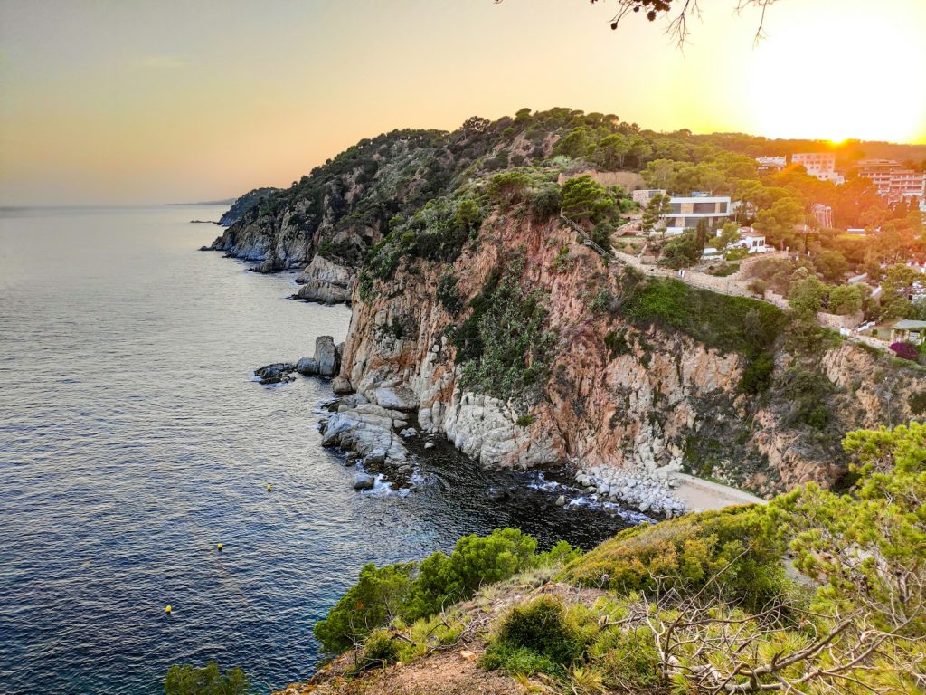 Fenyves sziklás földnyelv a tengerben naplementekor Tossa de Mar mellett