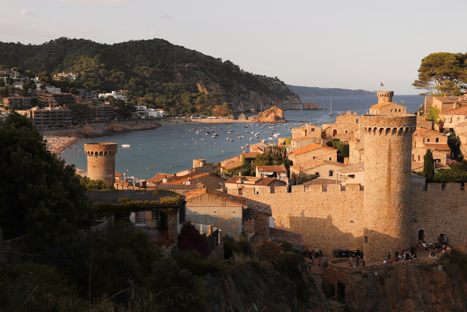 Tossa de Mar középkori városfalai és tornyai naplementekor, háttérben az öböl